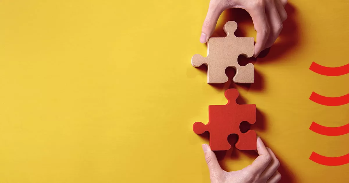 Two hands holding a red and yellow puzzle piece, symbolizing teamwork and collaboration